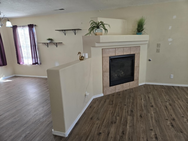 unfurnished living room featuring a textured ceiling, wood finished floors, visible vents, baseboards, and a tiled fireplace