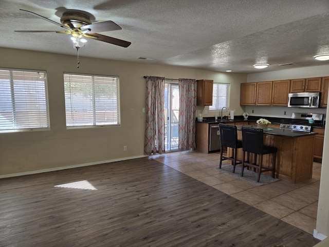 kitchen with dark countertops, light wood-style flooring, a kitchen island, appliances with stainless steel finishes, and a sink