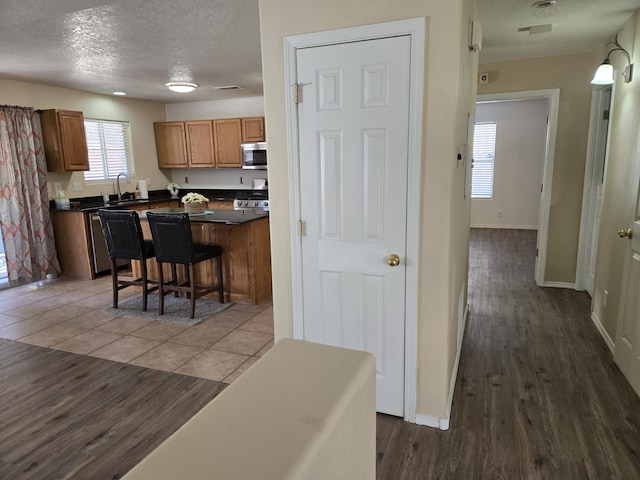 kitchen featuring light tile patterned floors, dark countertops, stainless steel microwave, a textured ceiling, and a sink