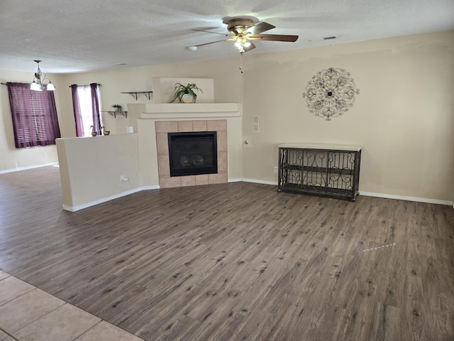 unfurnished living room with ceiling fan, a textured ceiling, wood finished floors, and a tile fireplace