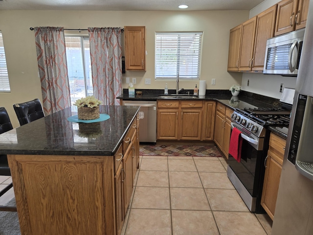 kitchen with dark stone counters, a kitchen island, stainless steel appliances, a sink, and light tile patterned flooring