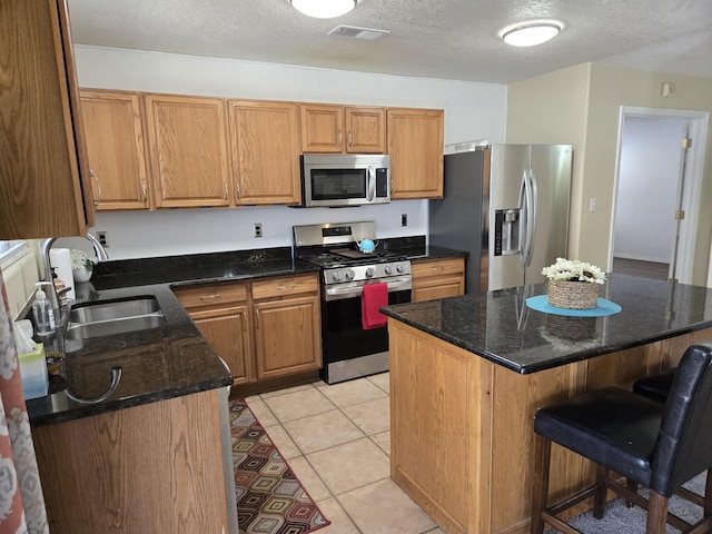 kitchen with light tile patterned floors, stainless steel appliances, a sink, visible vents, and a kitchen bar