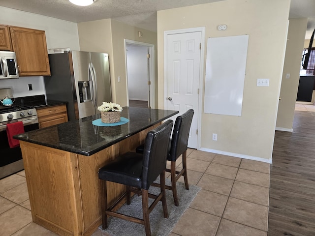 kitchen featuring light tile patterned floors, a textured ceiling, stainless steel appliances, a kitchen breakfast bar, and a center island