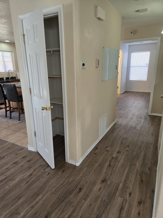 corridor featuring dark wood-type flooring, visible vents, a textured ceiling, and baseboards