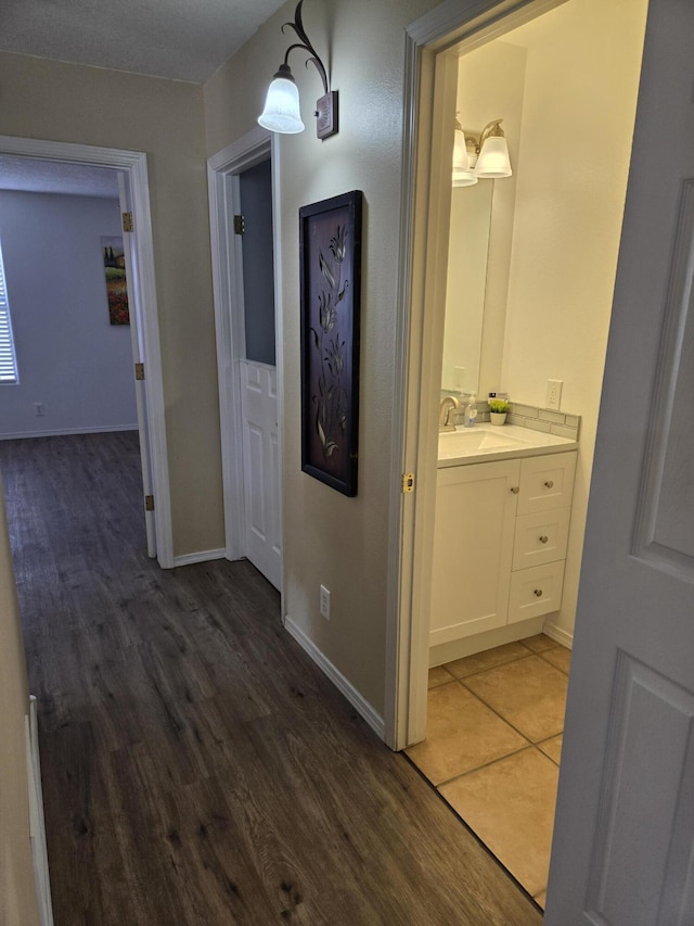 hallway with a sink, wood finished floors, and baseboards