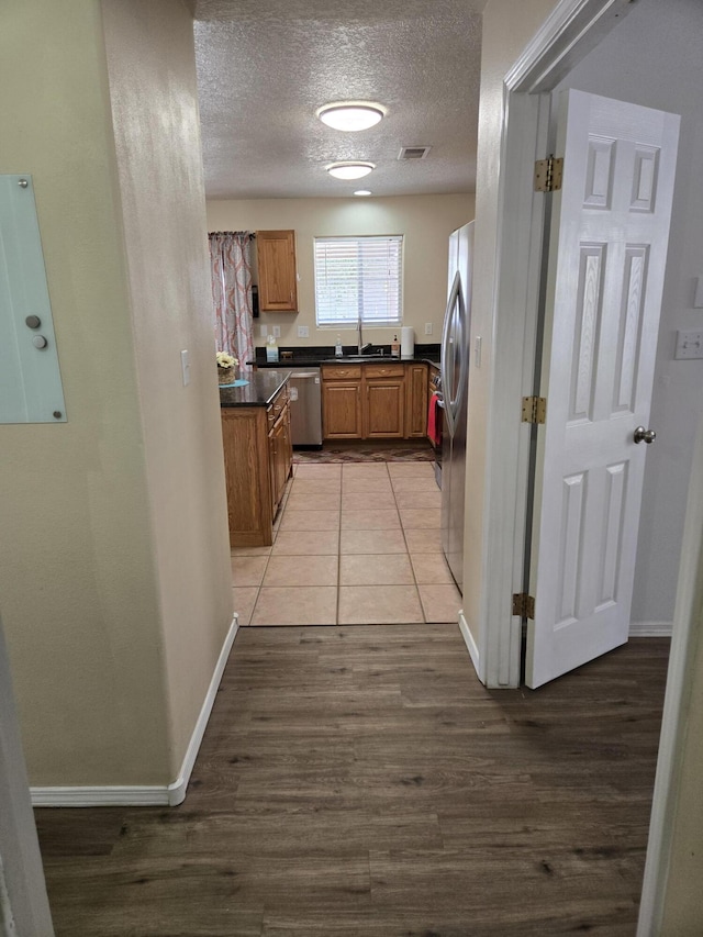 kitchen with dark countertops, visible vents, appliances with stainless steel finishes, brown cabinetry, and a textured ceiling