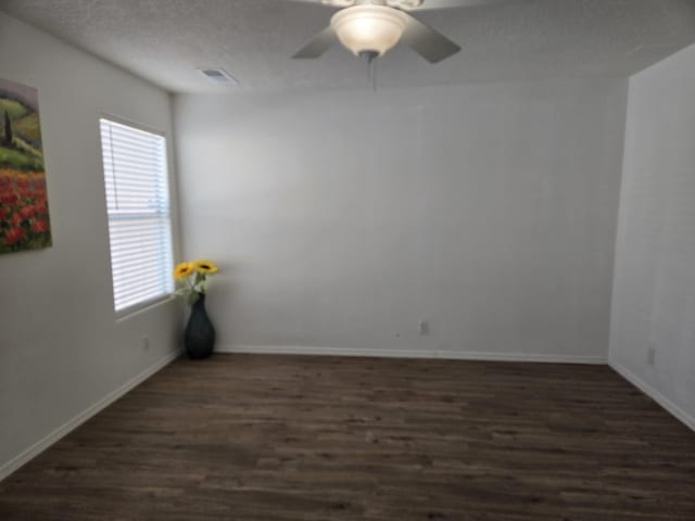 empty room featuring a textured ceiling, dark wood-type flooring, visible vents, and baseboards