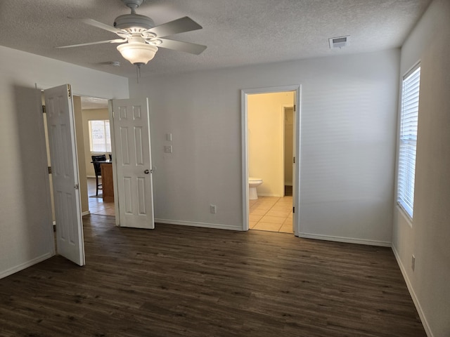 unfurnished bedroom featuring connected bathroom, a textured ceiling, visible vents, and dark wood-type flooring