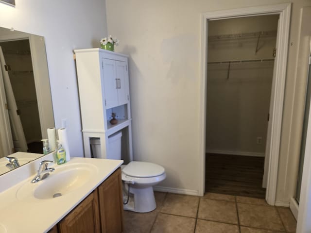 full bathroom with toilet, a walk in closet, vanity, and tile patterned floors