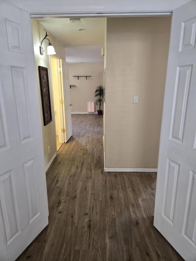 corridor with dark wood-style flooring and baseboards