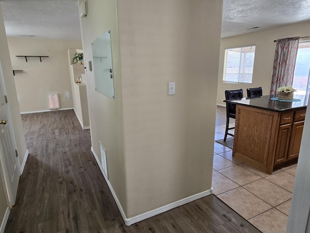 hall featuring a textured ceiling, visible vents, baseboards, light wood-type flooring, and electric panel