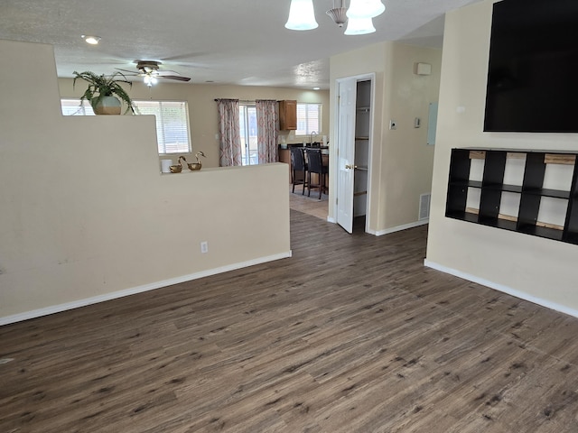 empty room with dark wood-style floors, visible vents, baseboards, and ceiling fan with notable chandelier