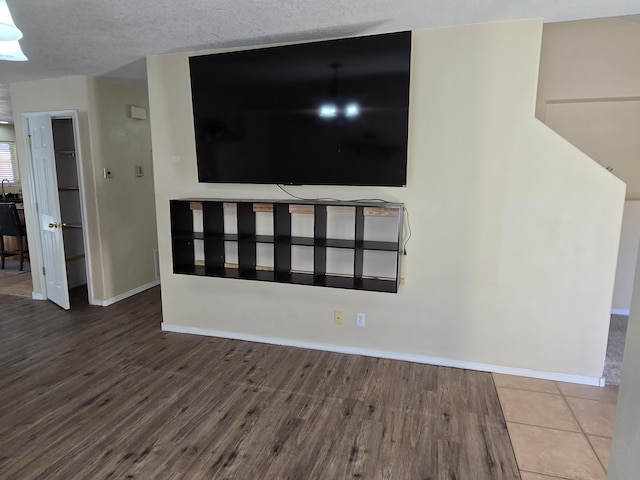 unfurnished living room with a textured ceiling, wood finished floors, and baseboards