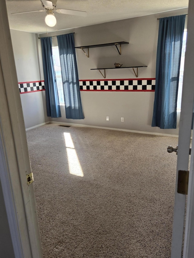 unfurnished room with carpet, visible vents, ceiling fan, and a textured ceiling