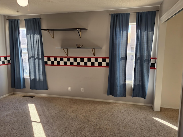 carpeted empty room featuring a textured ceiling, visible vents, and baseboards