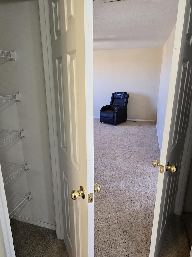 hall with carpet flooring, a textured ceiling, and baseboards