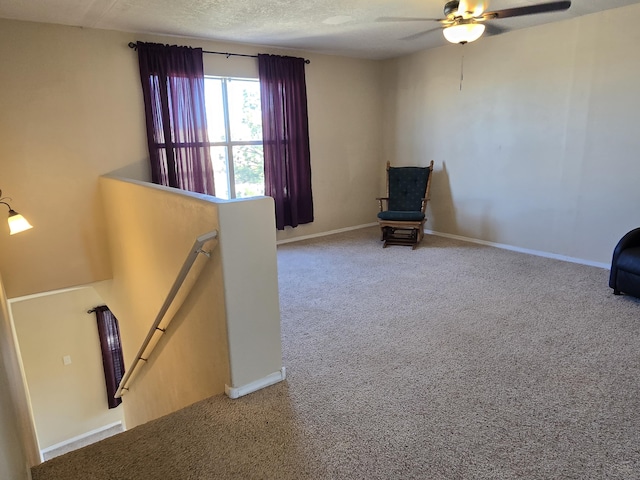 unfurnished room featuring carpet floors, a ceiling fan, a textured ceiling, an upstairs landing, and baseboards