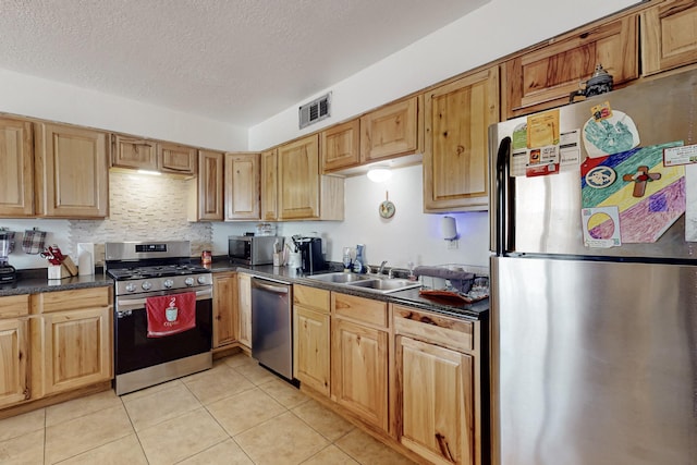 kitchen featuring light tile patterned floors, stainless steel appliances, dark countertops, visible vents, and a sink