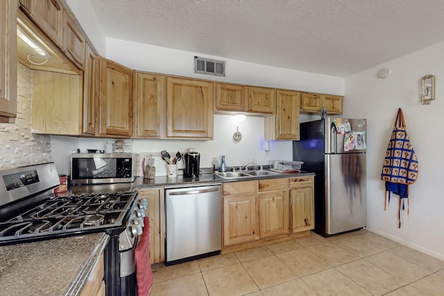 kitchen featuring appliances with stainless steel finishes, dark countertops, visible vents, and a sink