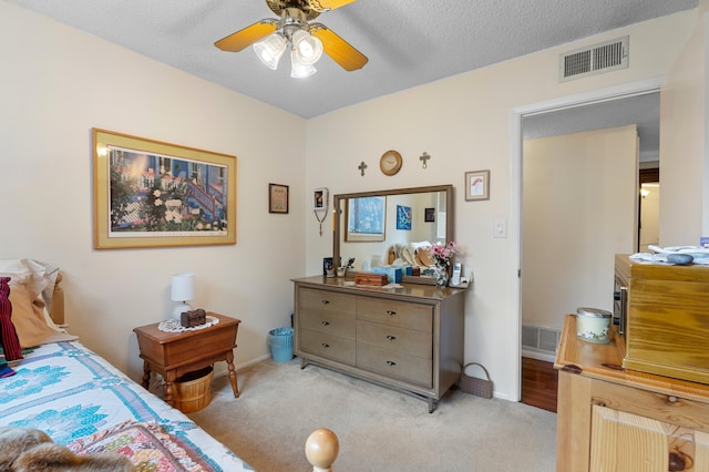 bedroom with a textured ceiling, light colored carpet, a ceiling fan, baseboards, and visible vents