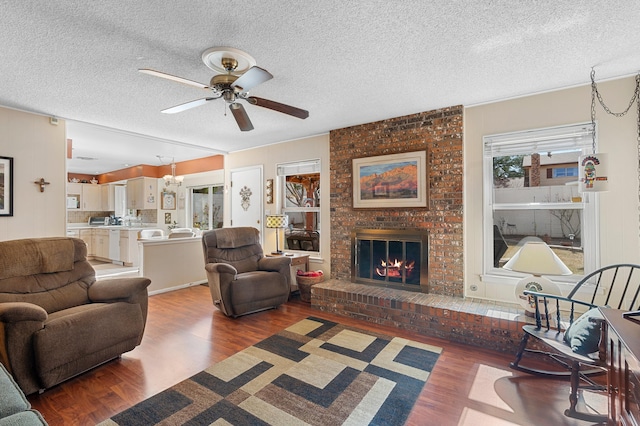 living room featuring a ceiling fan, a brick fireplace, a textured ceiling, and wood finished floors