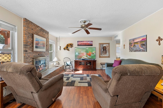 living area featuring a brick fireplace, ceiling fan, a textured ceiling, and wood finished floors