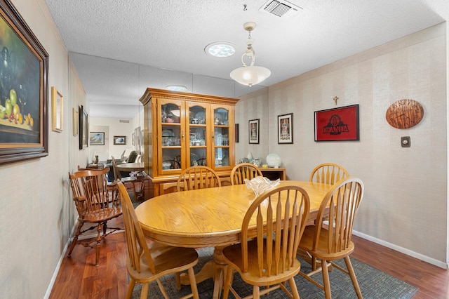 dining room featuring baseboards, a textured ceiling, visible vents, and wood finished floors