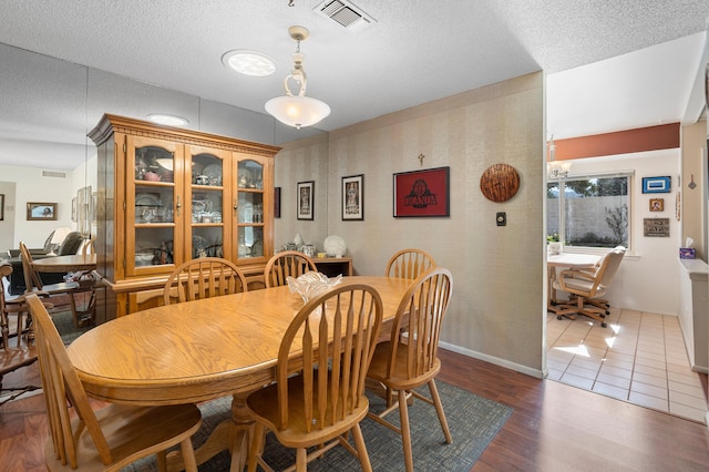 dining room with a textured ceiling, wood finished floors, visible vents, and wallpapered walls