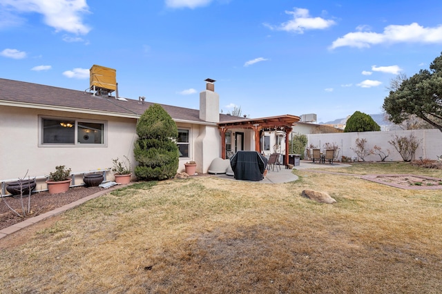 rear view of house featuring a patio, a chimney, fence, a yard, and stucco siding