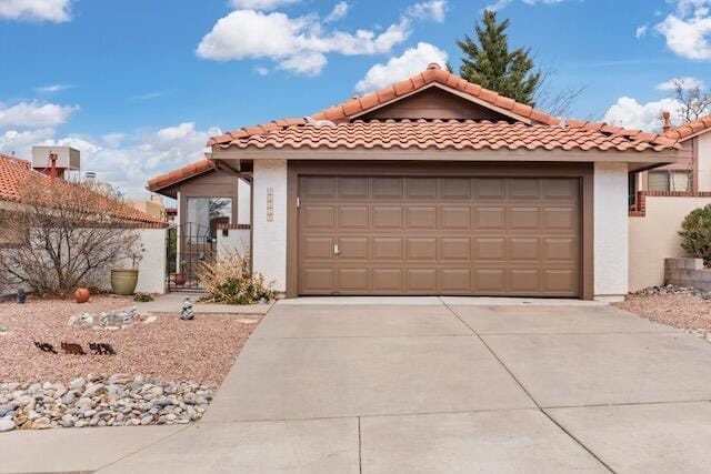 view of front of house featuring an attached garage, a tile roof, stucco siding, driveway, and a gate