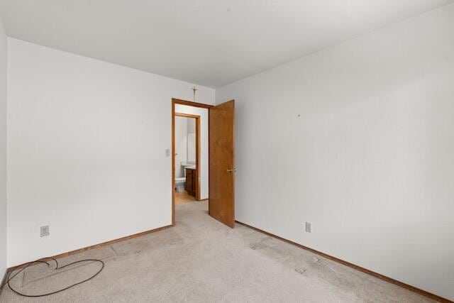 spare room featuring light colored carpet and baseboards