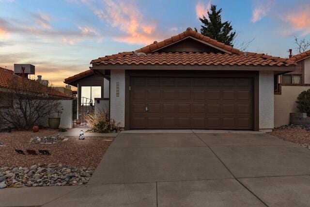 view of front of property featuring stucco siding, driveway, a tile roof, and an attached garage