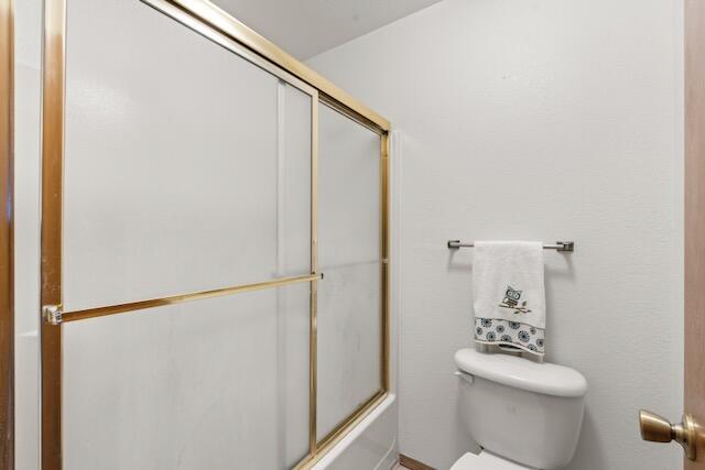 bathroom with toilet and shower / bath combination with glass door