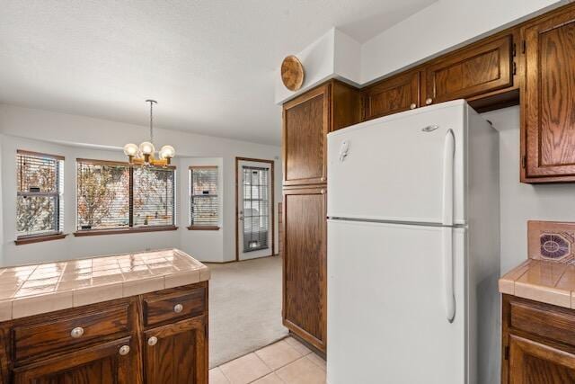 kitchen featuring tile counters, a chandelier, light carpet, freestanding refrigerator, and hanging light fixtures