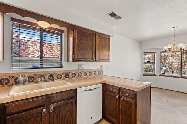 kitchen with visible vents, a peninsula, white dishwasher, a notable chandelier, and a sink