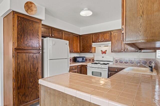 kitchen with white appliances, tile countertops, under cabinet range hood, and a sink