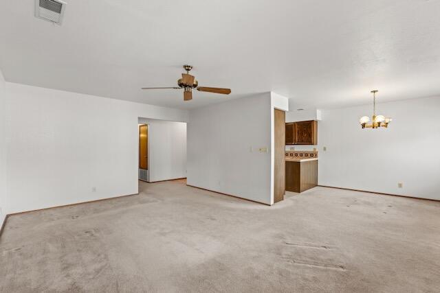 unfurnished living room featuring light carpet, visible vents, and ceiling fan with notable chandelier