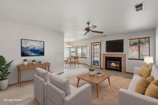 living room with visible vents, light carpet, a tile fireplace, and ceiling fan with notable chandelier