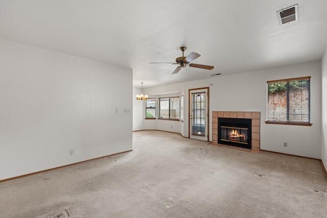 unfurnished living room with baseboards, visible vents, a tile fireplace, carpet flooring, and ceiling fan with notable chandelier