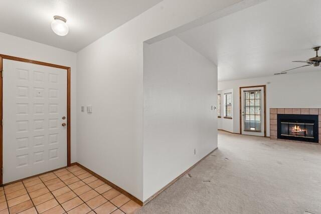 entrance foyer featuring a tiled fireplace, light tile patterned floors, baseboards, light colored carpet, and ceiling fan