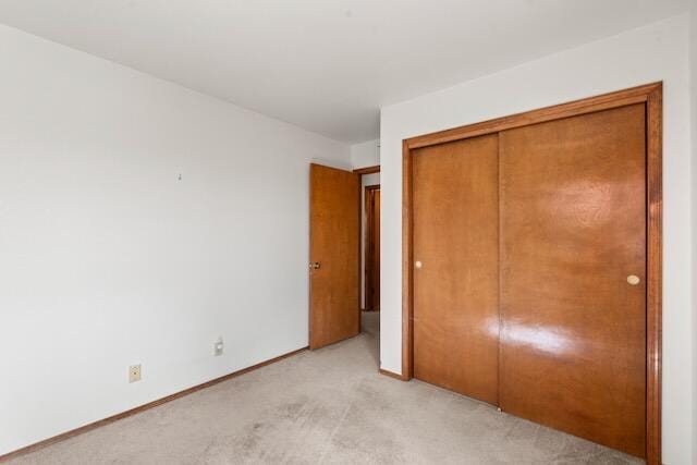 unfurnished bedroom featuring baseboards, a closet, and light carpet