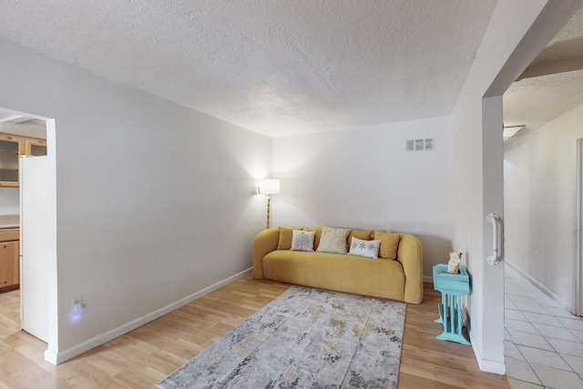 living area featuring a textured ceiling, light wood-type flooring, visible vents, and baseboards