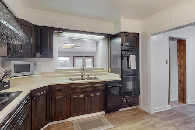 kitchen with wall chimney exhaust hood, light wood-style flooring, light countertops, black appliances, and a sink