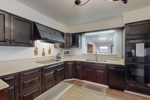 kitchen featuring light countertops, a sink, wall chimney range hood, and black appliances