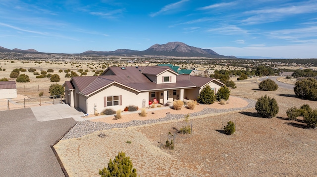 view of front of house featuring stucco siding, concrete driveway, a mountain view, fence, and metal roof