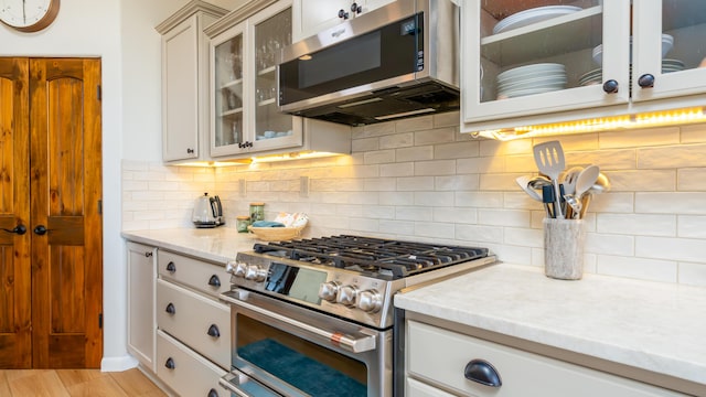 kitchen featuring tasteful backsplash, appliances with stainless steel finishes, light wood-style floors, glass insert cabinets, and light stone countertops