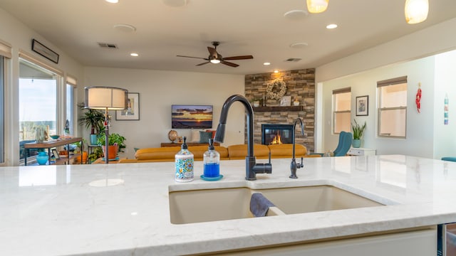 kitchen with visible vents, open floor plan, a sink, and a stone fireplace