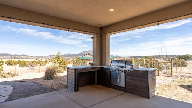 view of patio / terrace featuring grilling area, an outdoor kitchen, fence, and a mountain view