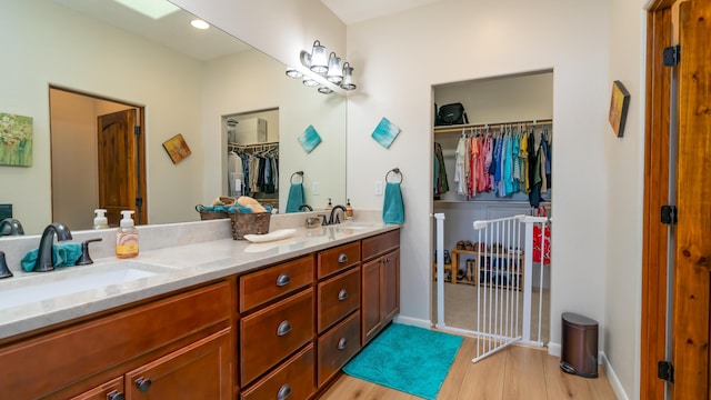 full bathroom featuring double vanity, a walk in closet, a sink, and wood finished floors