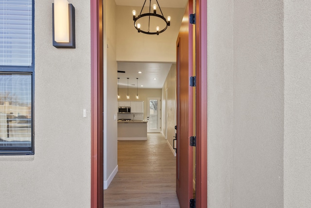 hallway with a notable chandelier, baseboards, and wood finished floors